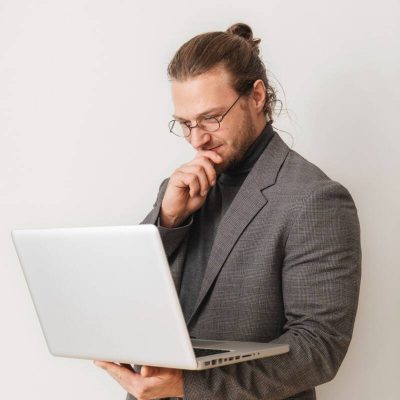 Mann mit Brille denkt nach während er auf Laptop schaut, steht für gewissenhafte Fachübersetzungen